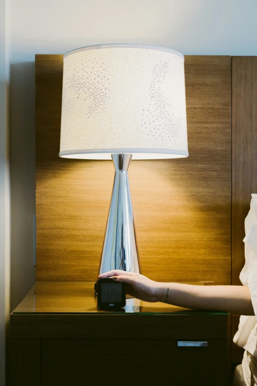 hand pointing towards table lamp in front of white bed