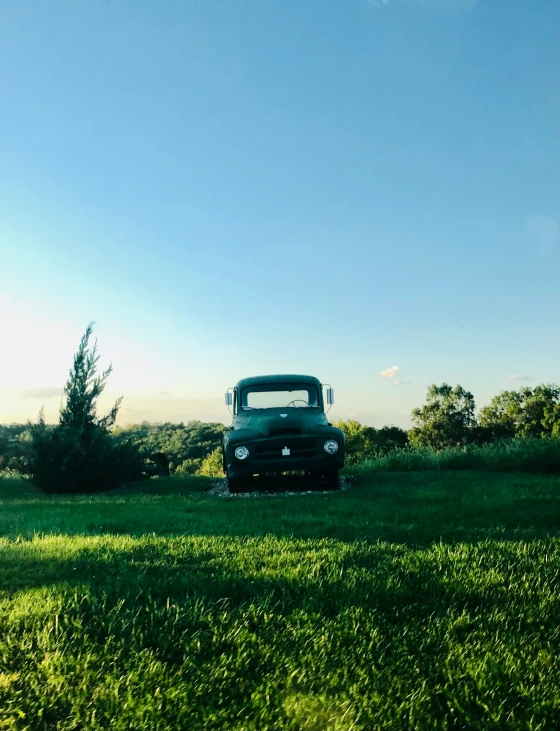 an old truck parked on the grass near trees