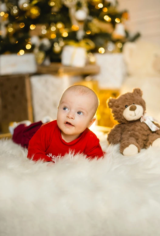 a baby is laying in front of a christmas tree and a teddy bear