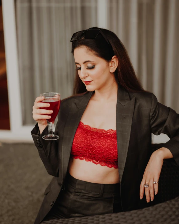 a woman in red , black blazer, and black shorts holding up a glass of wine
