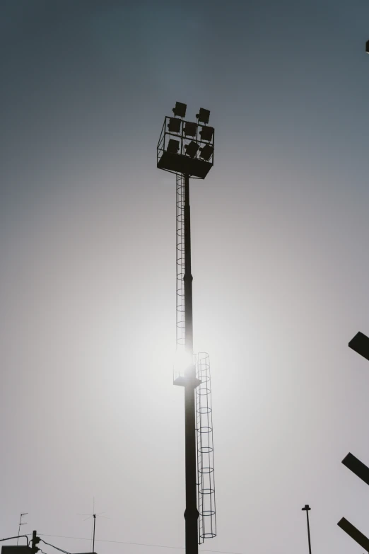 a tall light tower against the sky and the sun