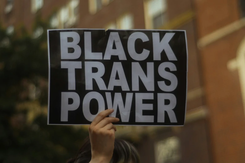 a person holding up a sign in the air with a large amount of words reading black transs power