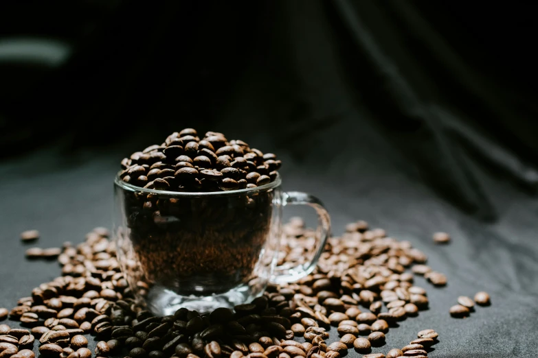 a glass mug filled with coffee beans on top of a black surface