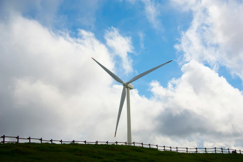 two wind turbines on top of a hill under a cloudy blue sky