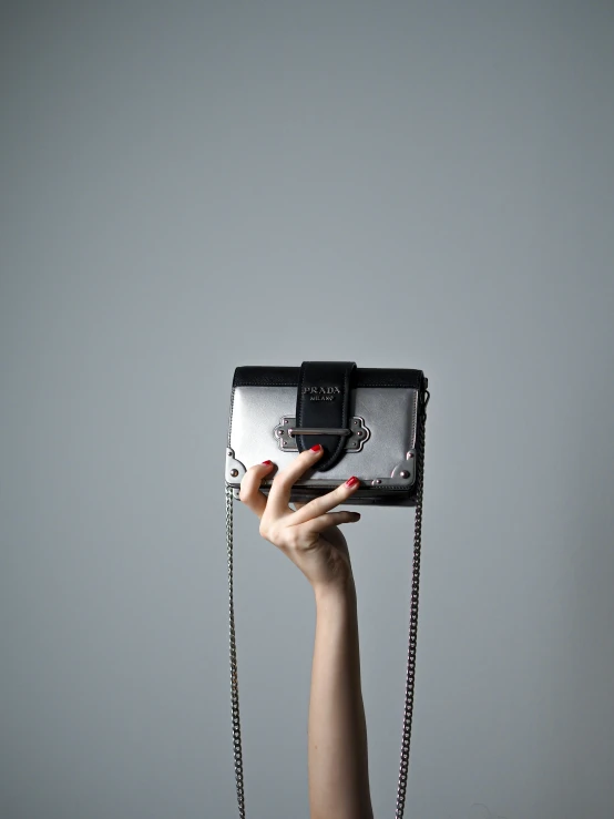 a woman's hand holding a black purse on top of a gray wall