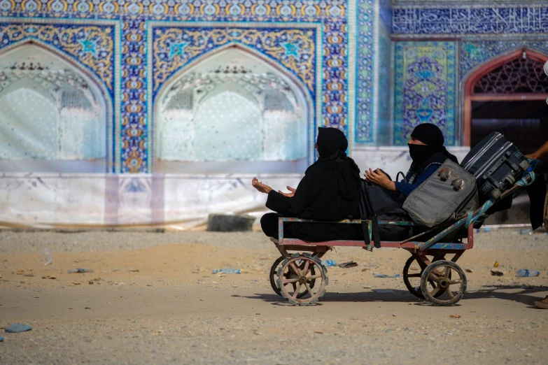 two women sit in a covered carriage near a blue wall