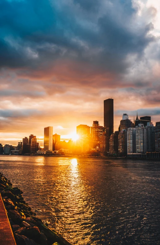 sun setting over the water next to a city skyline