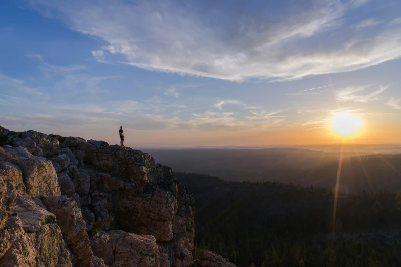 the person is on top of a rock with the sun setting in the background