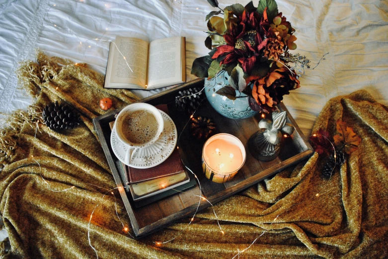 a tray with an open book, an empty mug of coffee and some candles on it