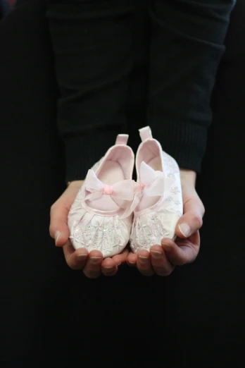 hands hold little white baby shoes with lace bows