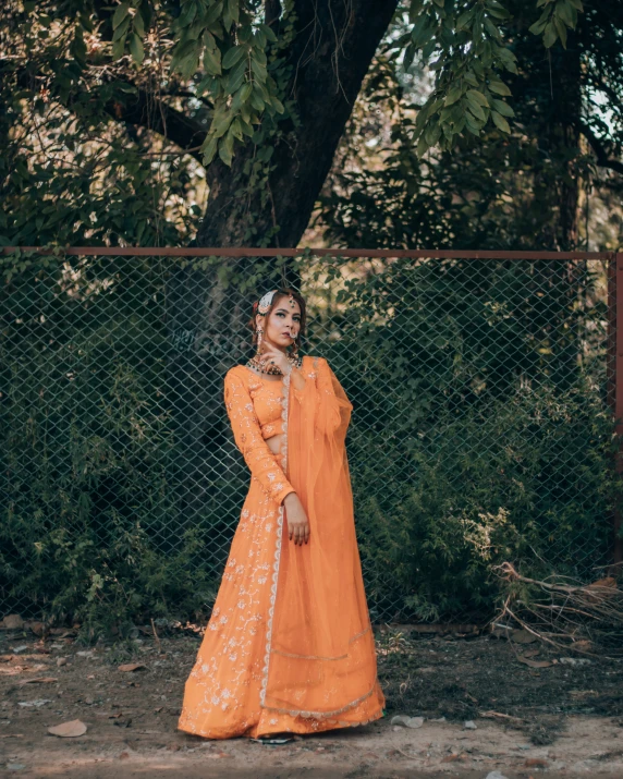 woman in orange dress leaning against chain link fence