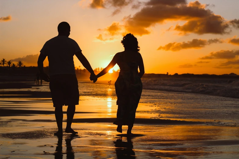 a man and woman walking down a beach holding hands