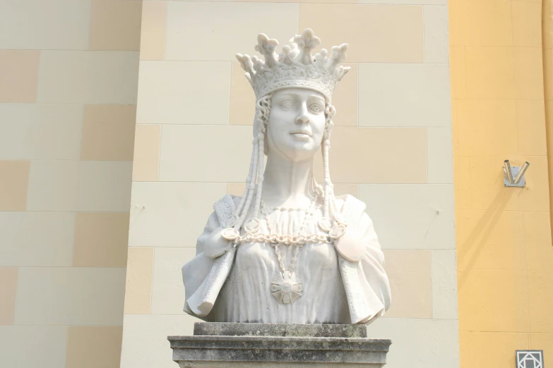 a statue of a woman wearing a tiara and holding a book is pictured on display in front of a building