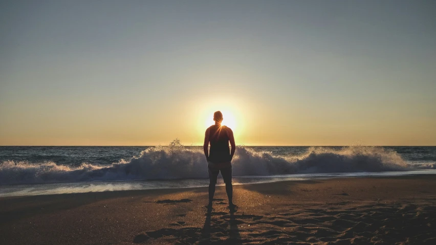 a man stands on the beach during a sunset