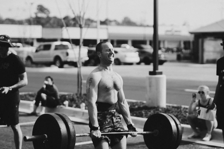 a man lifting a barbell while others watch from the road