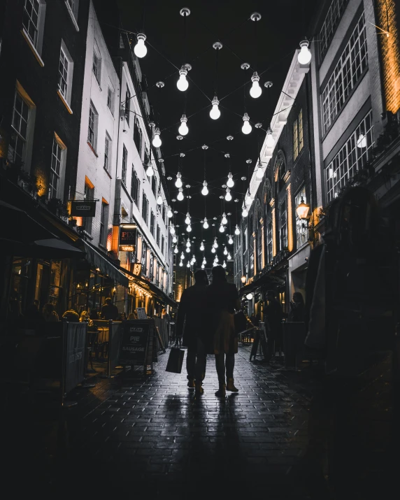 two people walking down an alley under lights