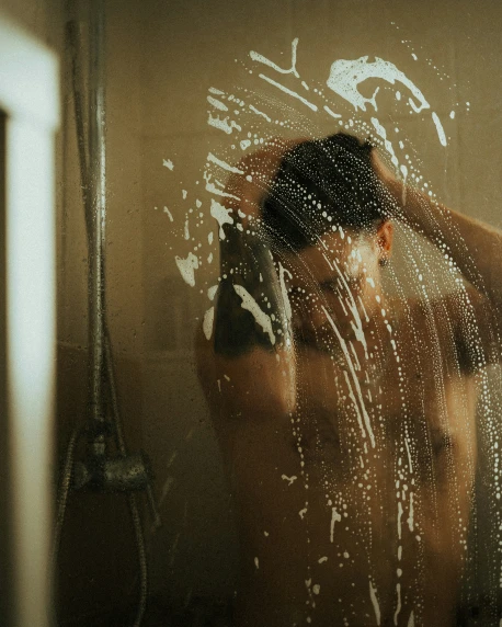 man standing in bathroom under shower with clear glass
