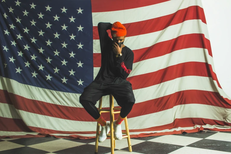 a man sitting on top of a wooden stool in front of a flag