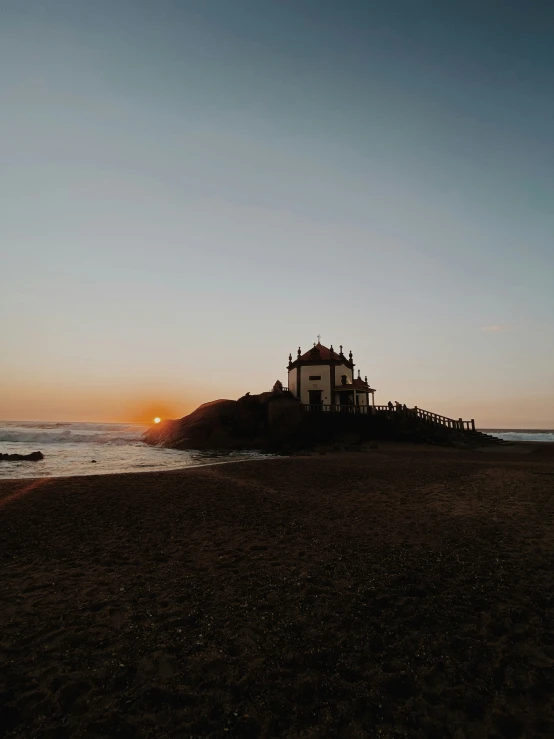 the sun is setting over the beach and a small building in the middle