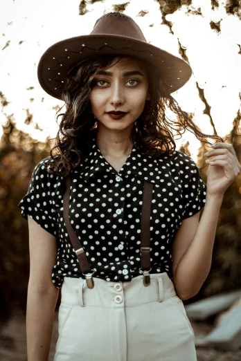 a girl wearing suspenders and a big hat poses for a picture