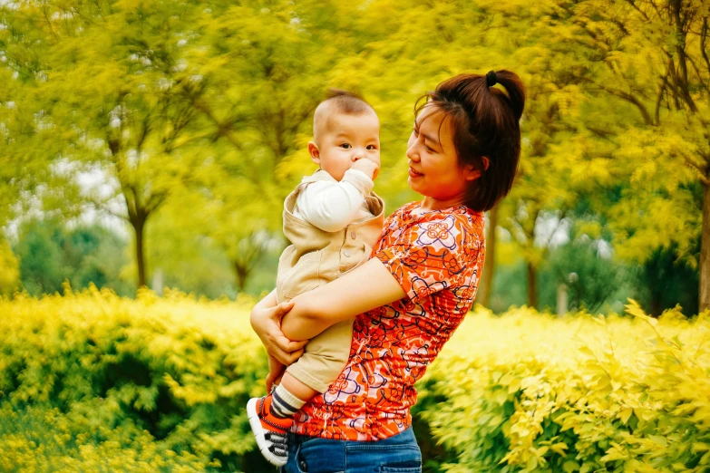 woman holding her baby girl in a park full of green leaves