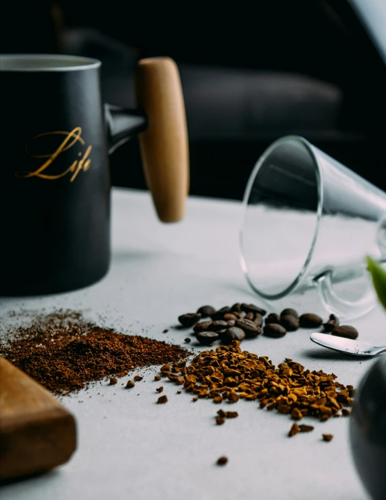 a table topped with a mug of coffee next to two spoons and some nuts