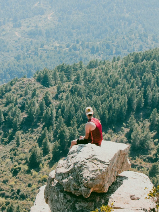 a man sitting on top of a rock with trees in the background