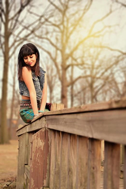 a girl with short hair and tight pants leans on a wooden fence