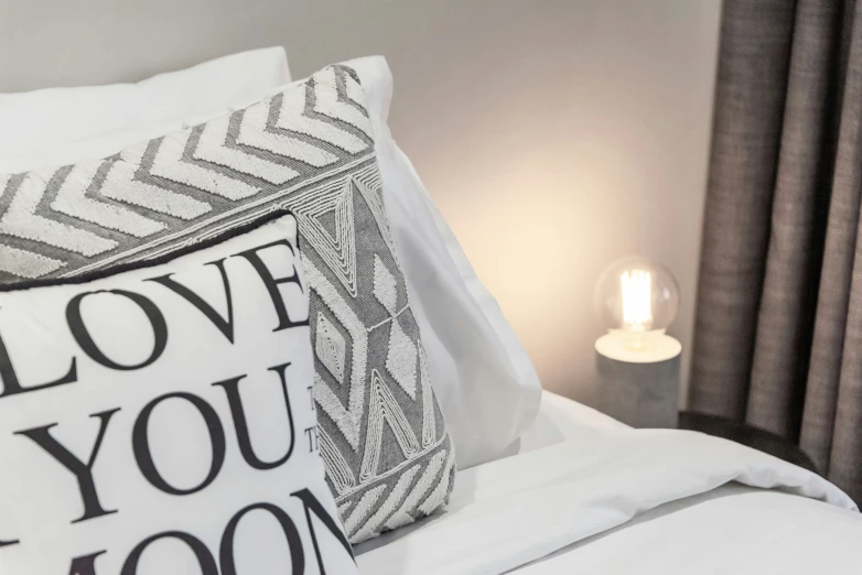 black and white love you too pillow sitting on top of a bed