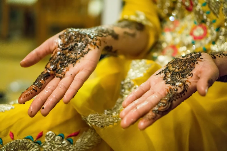 a woman in yellow clothing covered in gold glitters with her hands extended