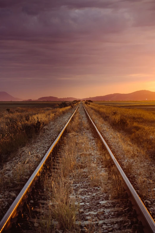 a train track in the middle of the field during sunset