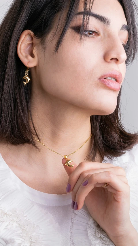 a woman wears a gold pendant and a white top