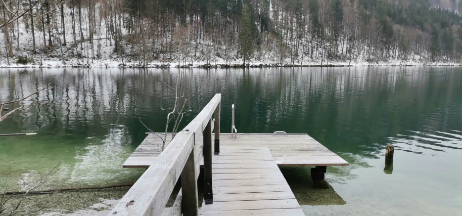 wooden dock at edge of water near snow covered mountain