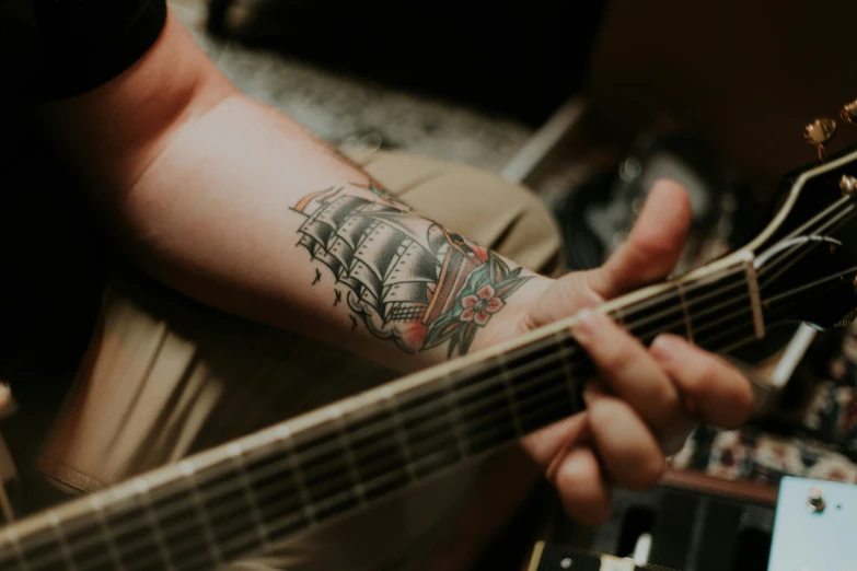 the person with the tattoo on their arm is playing a guitar