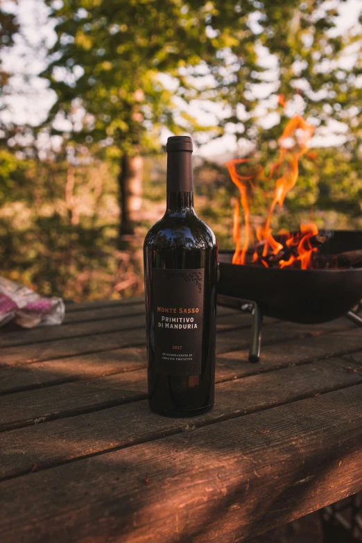 a bottle of wine next to an open fire pit