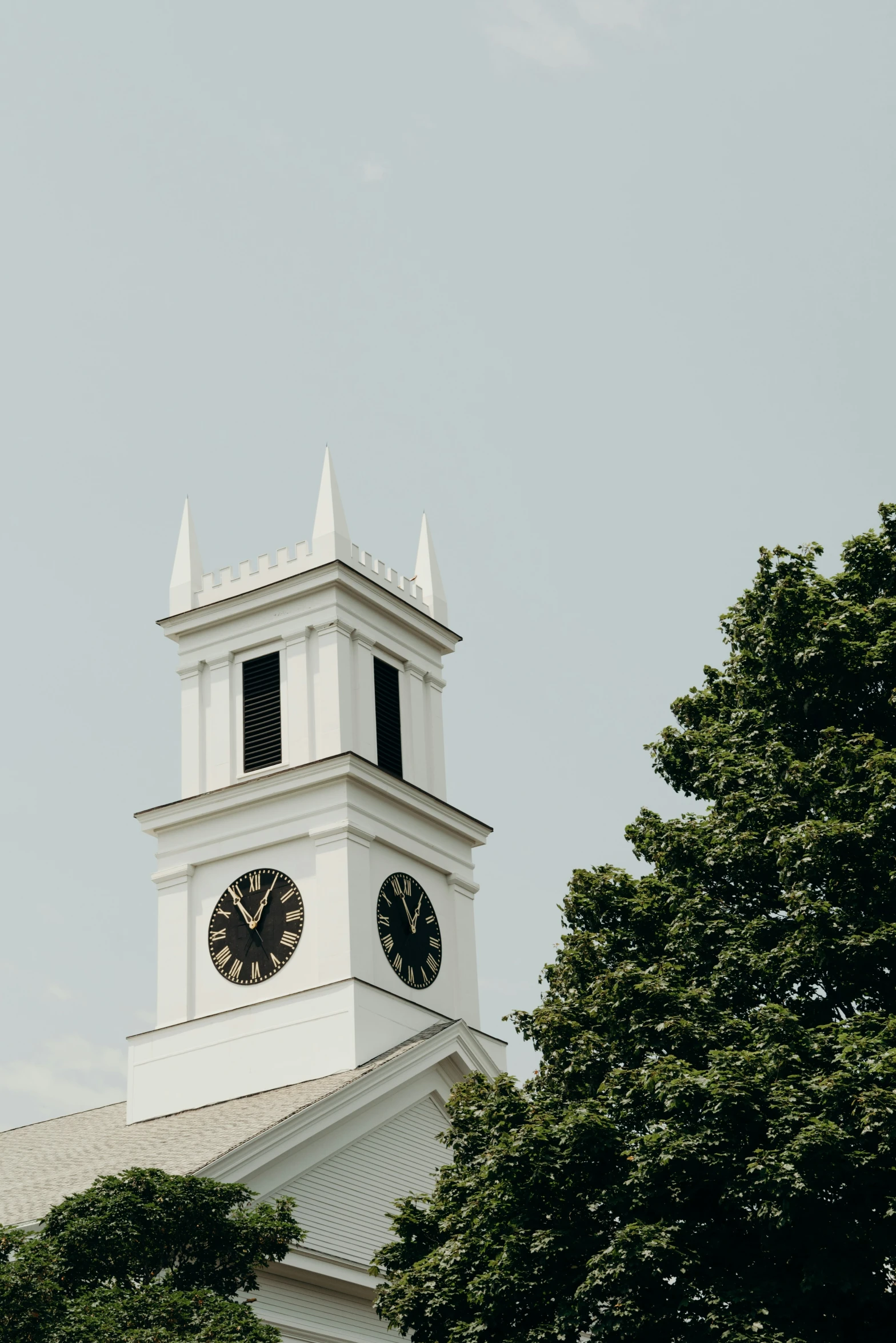 a white clock tower with trees behind it