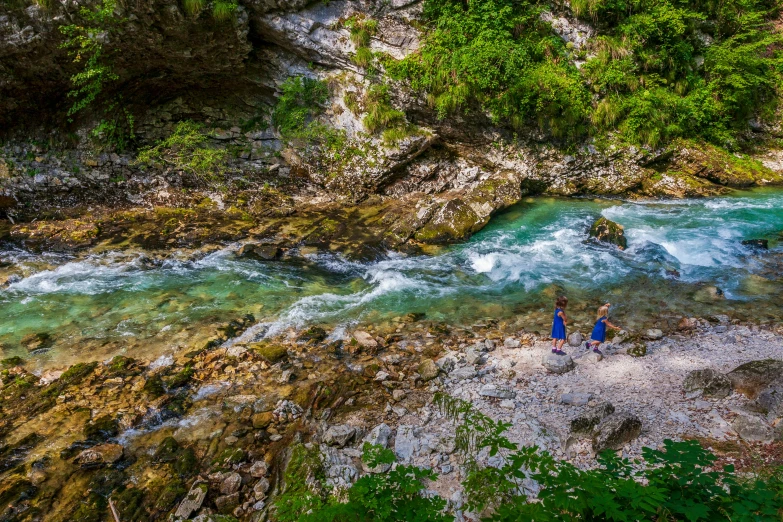 two people standing on a rock and next to a river