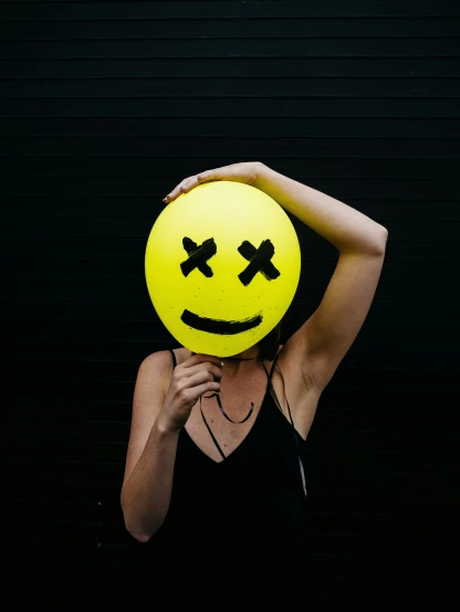 a woman holding up a yellow face balloon