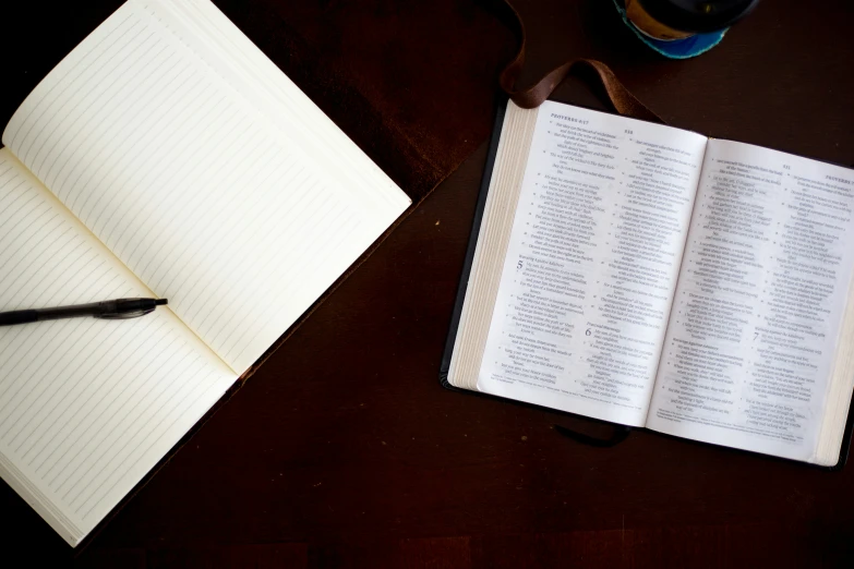 an open notebook, pen, and two glasses sitting on a table