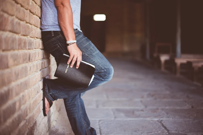 a man leaning up against a wall while wearing jeans and a white shirt