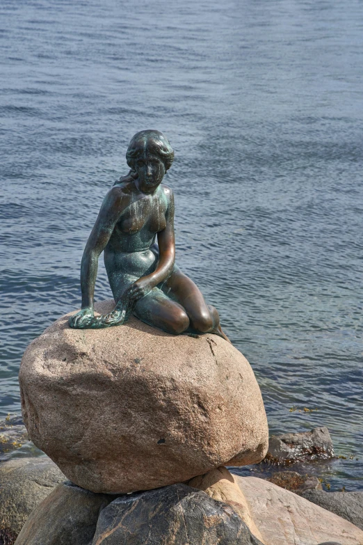 there is a small mermaid sitting on a rock