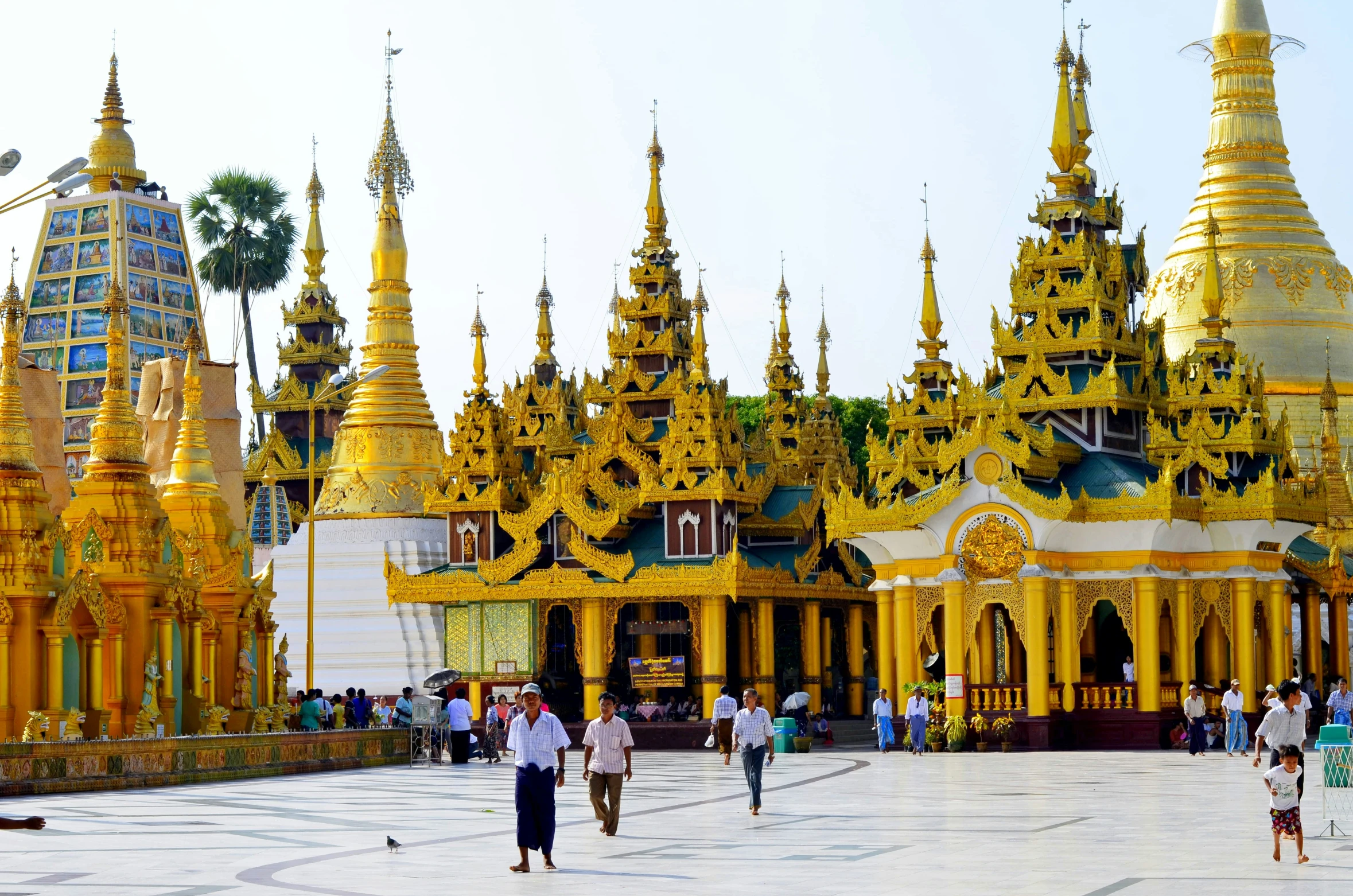 many gold decorated buildings in a plaza with people walking