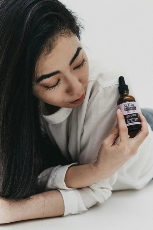 a woman wearing a white sweater and white boots sitting in front of a bottle of hair oil