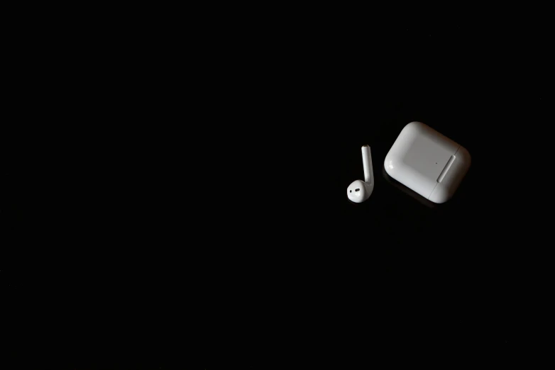 apple airpods with one earphone on it sitting in the dark