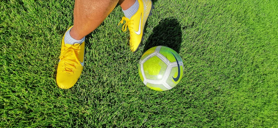 someone's legs resting on the grass and next to their soccer ball