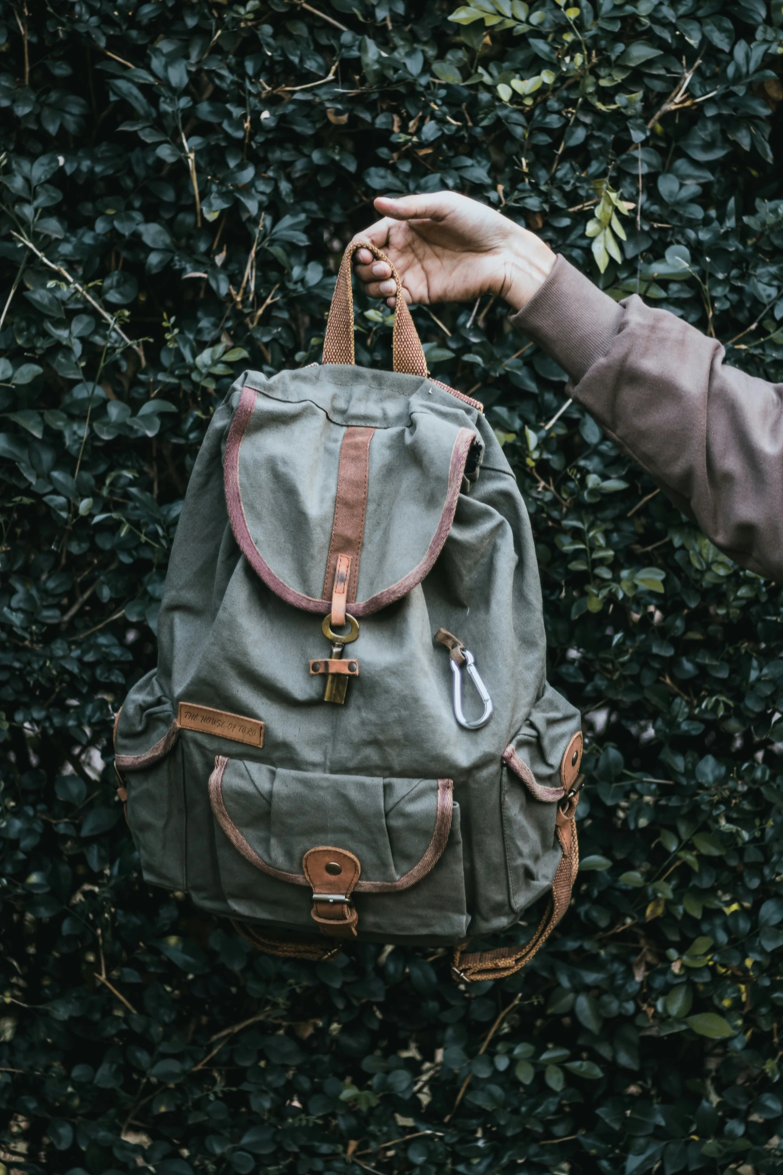 person holding up a backpack in front of some bushes