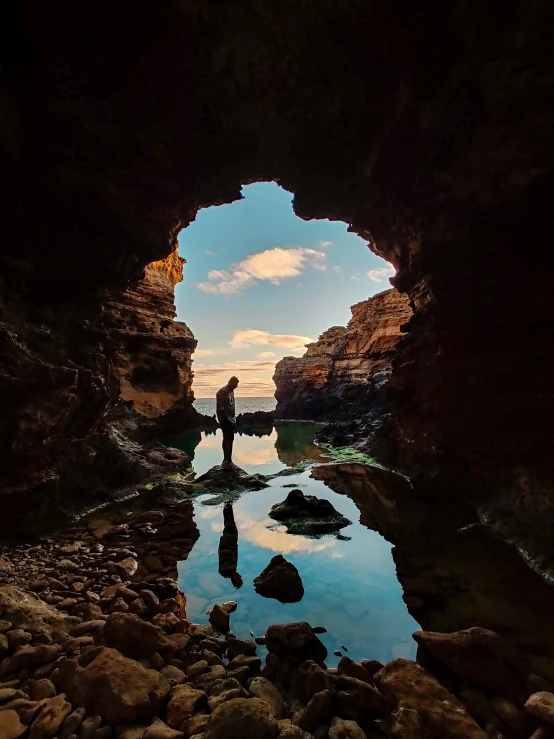 a person standing in a cave looking at the sun