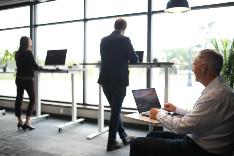 two people working at laptops, one sitting on a chair in an office