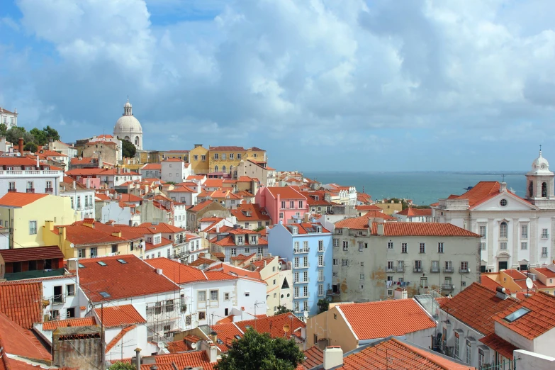 city with several buildings in it, orange roofs and a view of the sea
