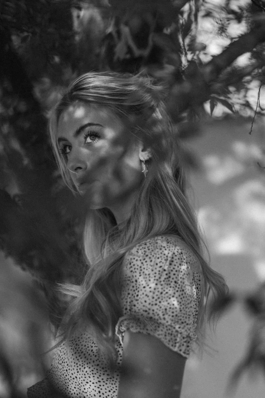 a woman stands in front of a tree, and looks away from the camera